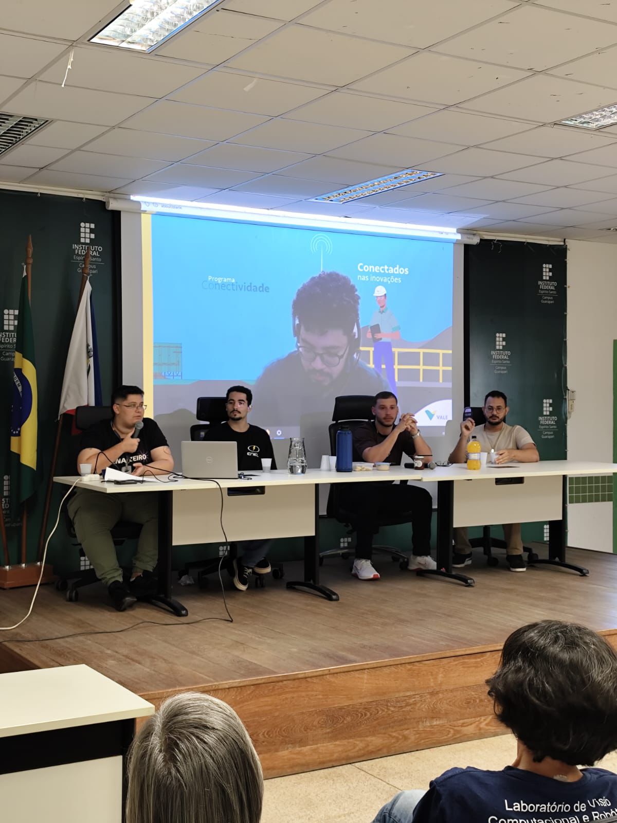 Quatro membros do Centro Acad&ecirc;mico de Engenharia El&eacute;trica discursam, sentados, no Audit&oacute;rio do Campus Guarapari